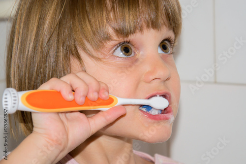 Kid girl brushing teeth in bathroom photo