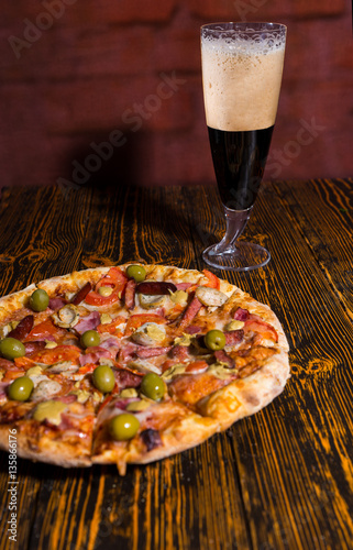 Tasty pizza on wooden table near a glass of dark beer
