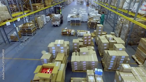 Worker in loader transporting goods cardboard boxes in warehouse storage HD video. Forklift rides between shelves. Man working on lift truck