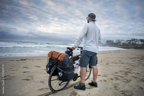 Young man with packed bicycle on beach