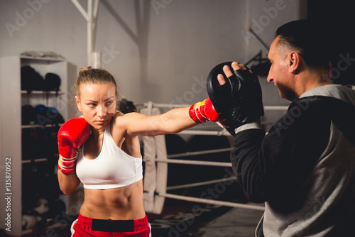 Woman boxer hitting training mitts held by her coach