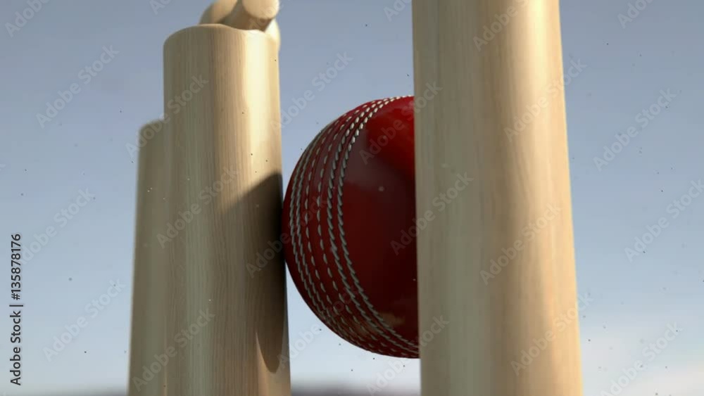 An ultra motion close up of a red leather stitched cricket ball hitting wooden wickets with dirt particles emanating from the impact in the day