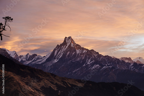 Beautiful landscape of Mount Machapuchare covered with snow and ice and illuminated with pink sunlight. Craggy snowy peak rising above desolate valley. Frosty winter morning high in mountains