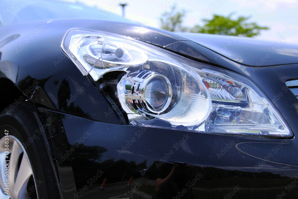 Headlight and body of a black car damaged in collision
