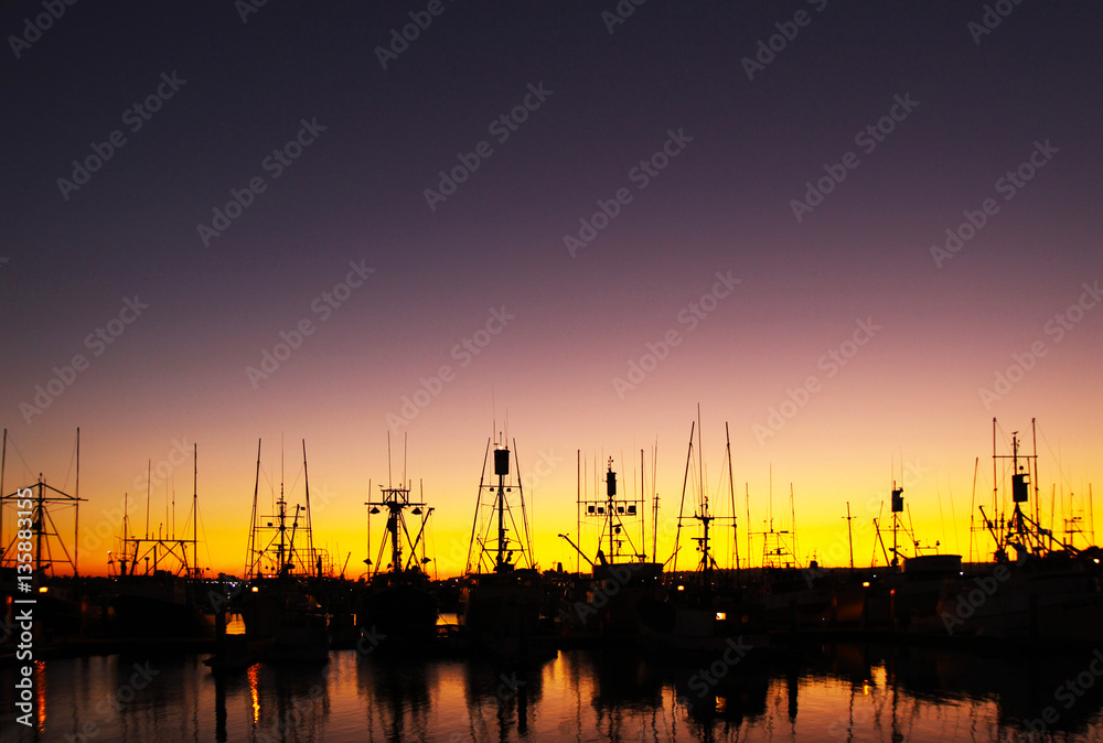 Sunset silhouette of docked boats in clear sky and reflection