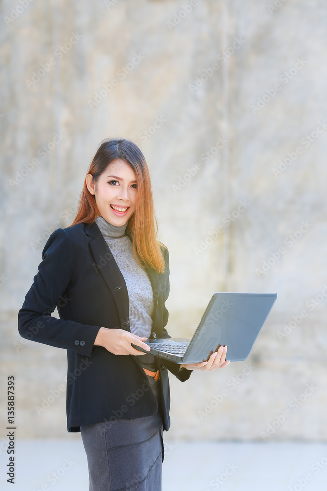 Asian business woman standing and smiling, The beautiful business women hold laptop, brown wall background Asian business woman standing and smiling, The beautiful business women hold laptop, brown wall background
