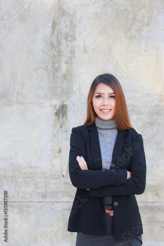 Business woman standing cross one's arm, Asian people young beautiful businesswoman smile and wear shirt black suit, space brown wall background