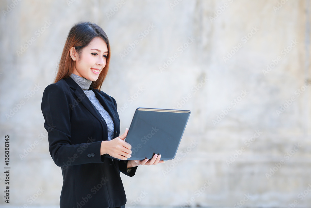 Asian people businesswoman standing and smiling, The beautiful business women hold laptop and smiling , brown wall background Asian people businesswoman standing and smiling, The beautiful business women hold laptop and smiling , brown wall background