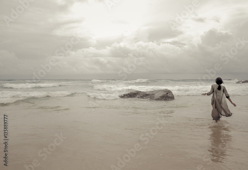 Canvas-taulu Elegant woman walking alone in the sea attracted by the divine light of sky, in