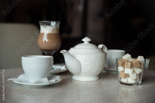 Teapot, two cups, sugar bowl and glass of shake on the table