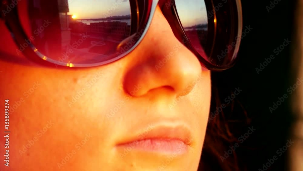 Close up of view pretty woman's face in sunglasses, standing at window and holding smartphone takes picture on sunset in the city background. That reflected in her sunglasses. 3840x2160 Close up of view pretty woman's face in sunglasses, standing at window and holding smartphone takes picture on sunset in the city background. That reflected in her sunglasses. 3840x2160