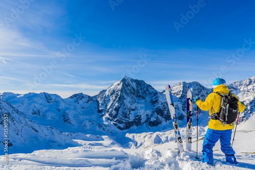 Mountaineer backcountry ski resting along a snowy ridge with ski
