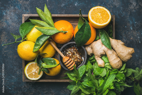Ingredients for making immunity boosting natural drink. Lemons, oranges, mint, ginger, honey in wooden box over plywood background, top view. Clean eating, healthy lifestyle, detox, dieting concept photo