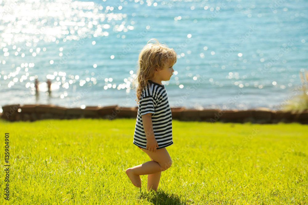 Fototapeta premium Cute baby boy in striped tshirt walks on green grass