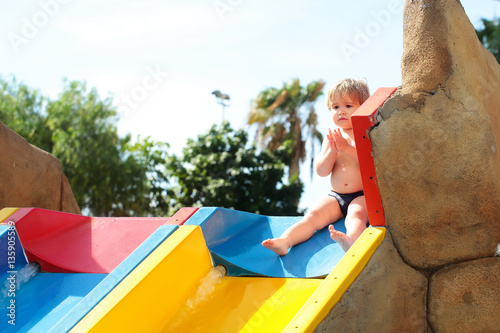 Scared cute baby boy sits on top of waterslide