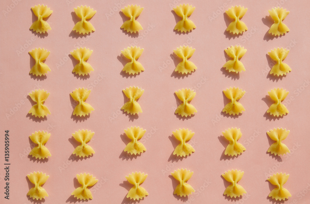 Maсaroni or pasta bow shape in row on pink background Maсaroni or pasta bow shape in row on pink background