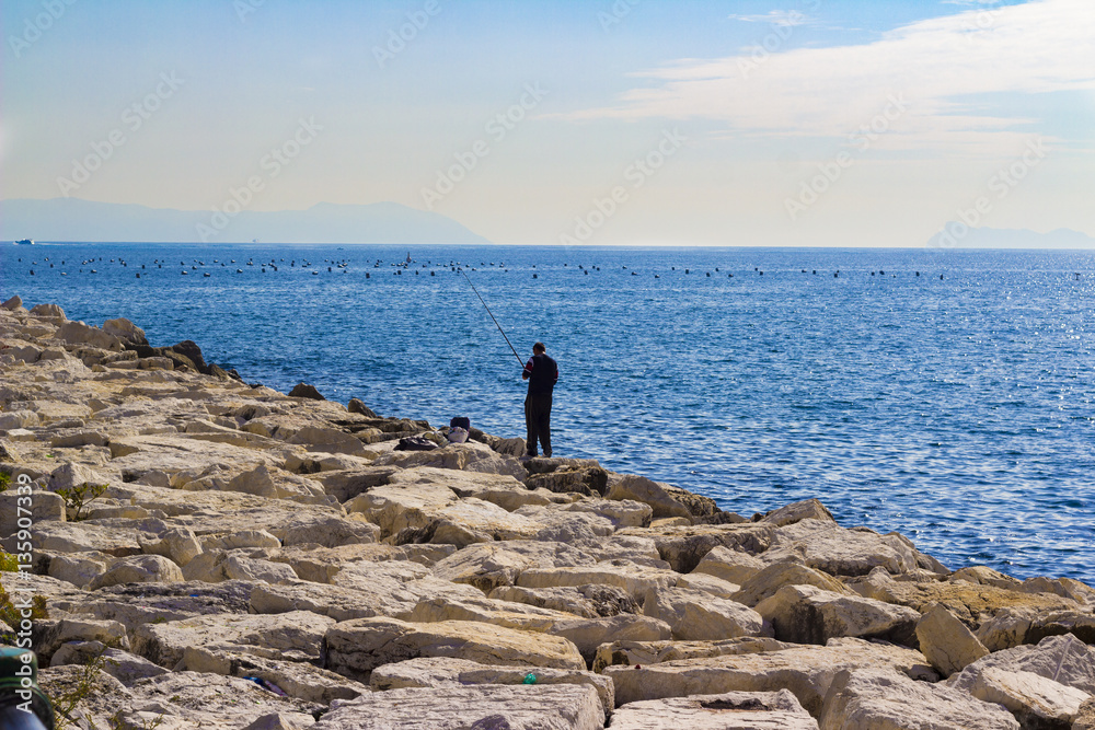 alone fisherman with rod on the rocks, Gulf of Naples, Italy