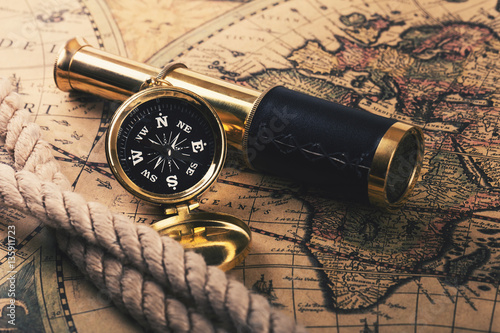 adventures concept - vintage compass and spyglass on old world map