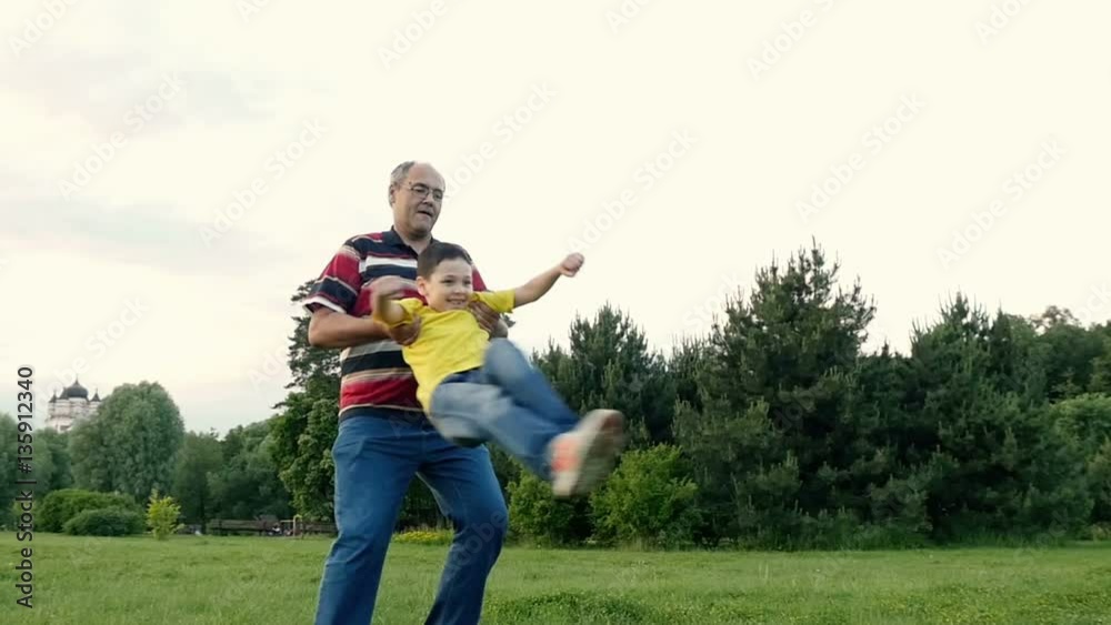 Uncle spinning his smiling nephew keeping him under armpits. Slow motion Uncle spinning his smiling nephew keeping him under armpits. Slow motion