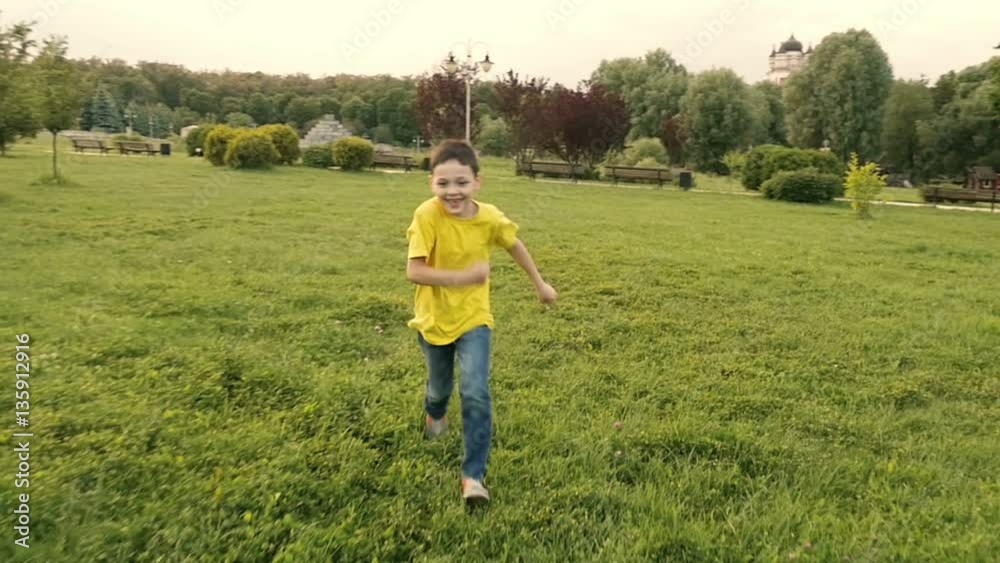 Smiling fine boy running through well trimmed grass in park zone. Slow motion Smiling fine boy running through well trimmed grass in park zone. Slow motion