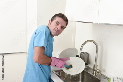 young lazy house cleaner man washing the dishes and cleaning the kitchen in stress and desperate