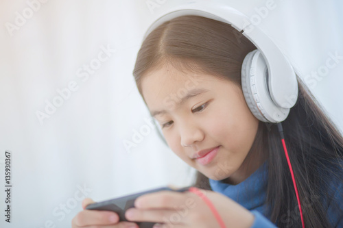 Pretty Asian girl using headphone for listen music by smartphone on the bed in her bedroom