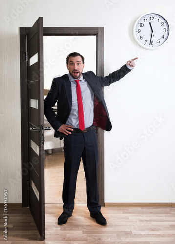 Indignant businessman pointing at the wall clock