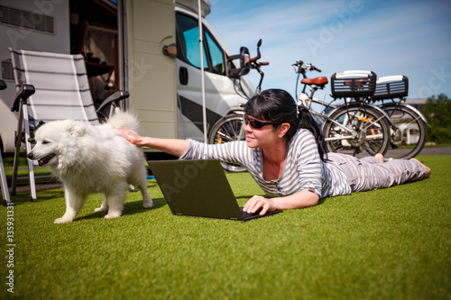 Woman on the grass with a dog looking at a laptop