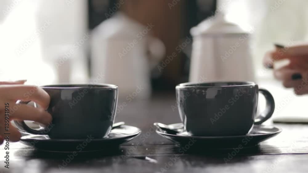 Two women put a cup of tea at same time in cafe - cropped video