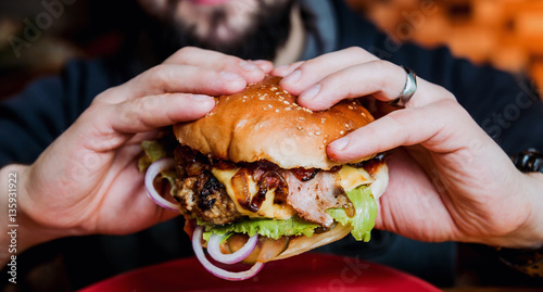 Fotografia, Obraz Young man eating a cheeseburger.
