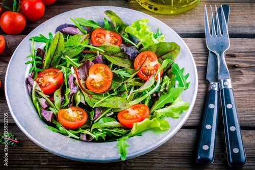 Fresh salad with mixed greens and cherry tomato on wooden background