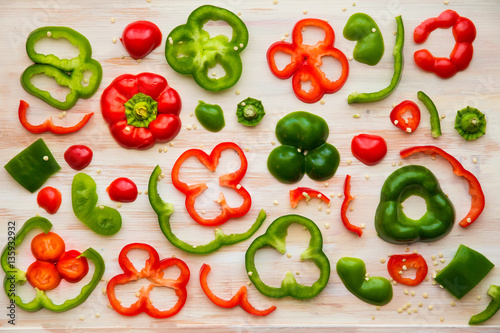 Food styling image design of red and green bell pepper slices on white wooden cutting board.