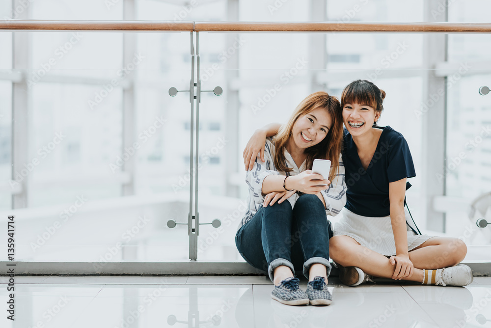 Obraz premium Young happy Asian girls best friends laugh and smile while having fun with smart phone mobile indoor.