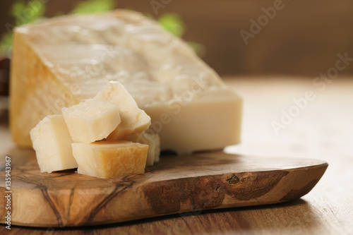 hard parmesan cheese cubes on olive cutting board, closeup photo