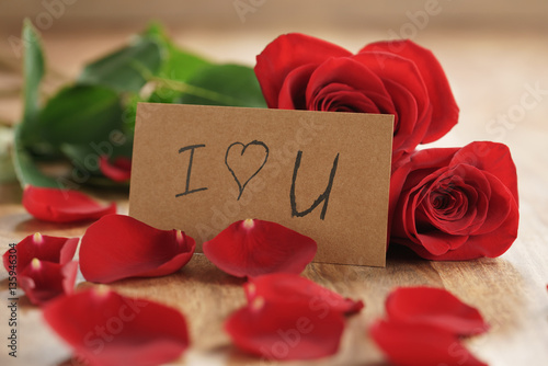 three red roses and petals on old wood table with i love you paper card, romantic background