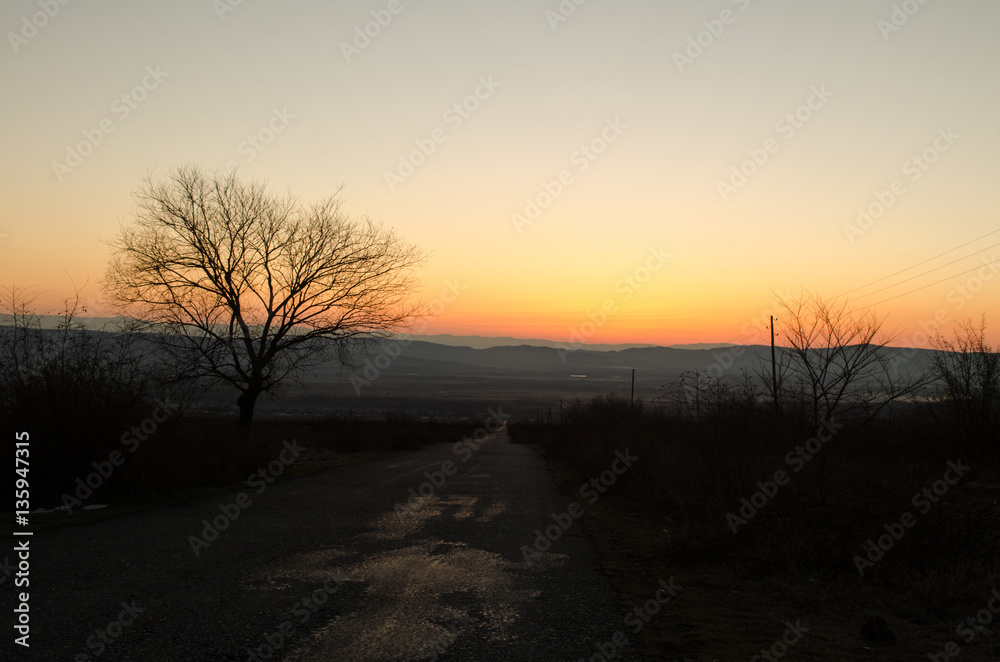 Autumn or winter landscape with road and trees. The gold light beams sunset. On a background of mountains and the sky with clouds. Azerbaijan Caucasus Autumn or winter landscape with road and trees. The gold light beams sunset. On a background of mountains and the sky with clouds. Azerbaijan Caucasus