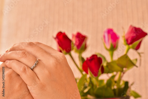Wedding ring in woman hands with red and pink rose background, V