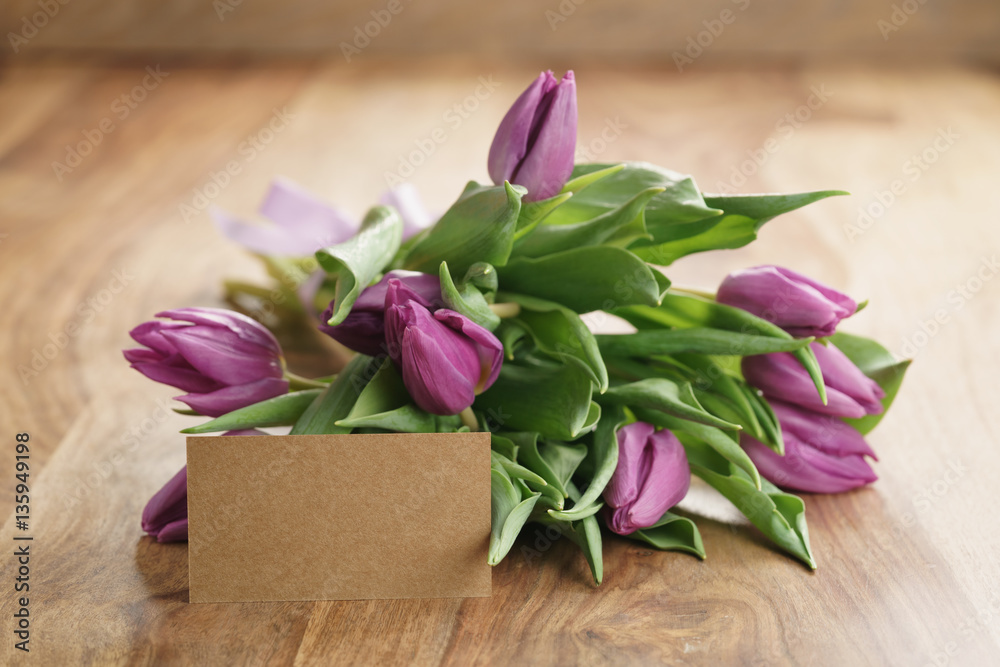 bouquet of purple tulips on wood table with empty paper card, shallow dof