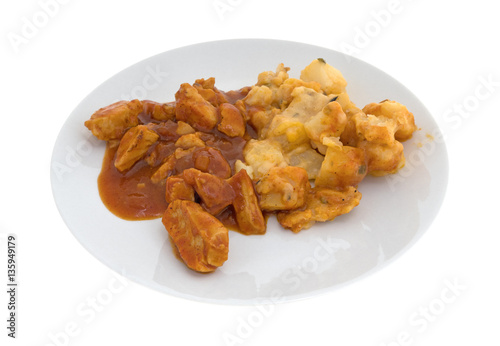 Plate with chicken chunks in barbecue sauce plus potatoes isolated on a white background.