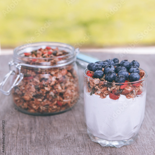 Breakfast in the garden: coconut yogurt topped with grain free  granola made with mixed nuts, seeds, raisins, with blueberries on the top, selective focus photo