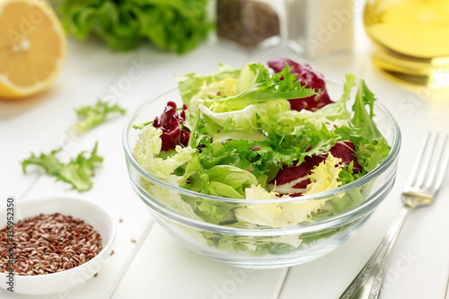 Mixed salad of iceberg, radiccio, endive, cabbage with flax seeds, oil and lemon on white wooden background.