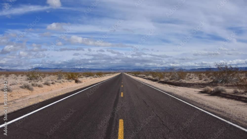 Time lapse clouds floating over two lane desert highway with vanishing perspective on sunny day Time lapse clouds floating over two lane desert highway with vanishing perspective on sunny day