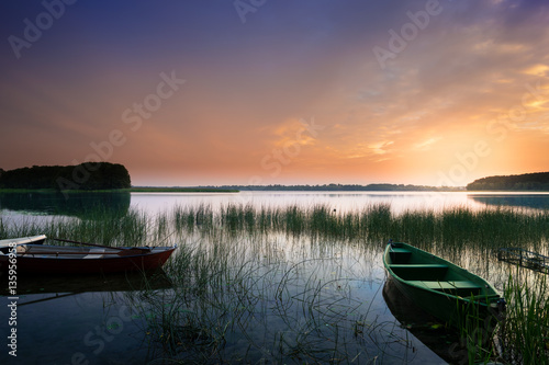 Rowing boat floating on the calm depths of the Lake Lasmiady. Just the sun rises. Masuria, Poland.