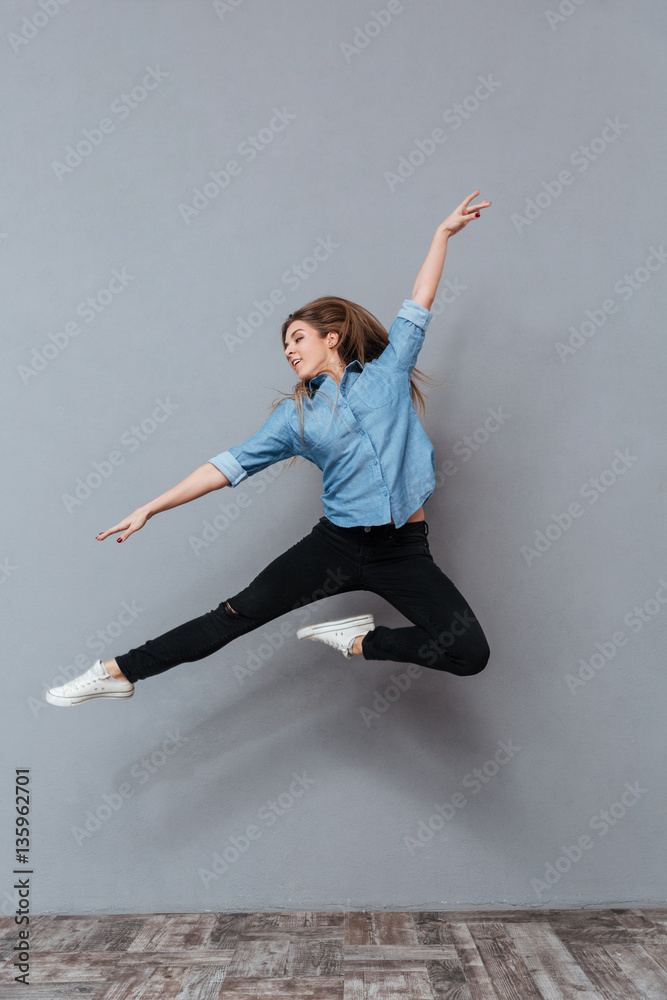 Full length portrait of woman in shirt jumping in studio