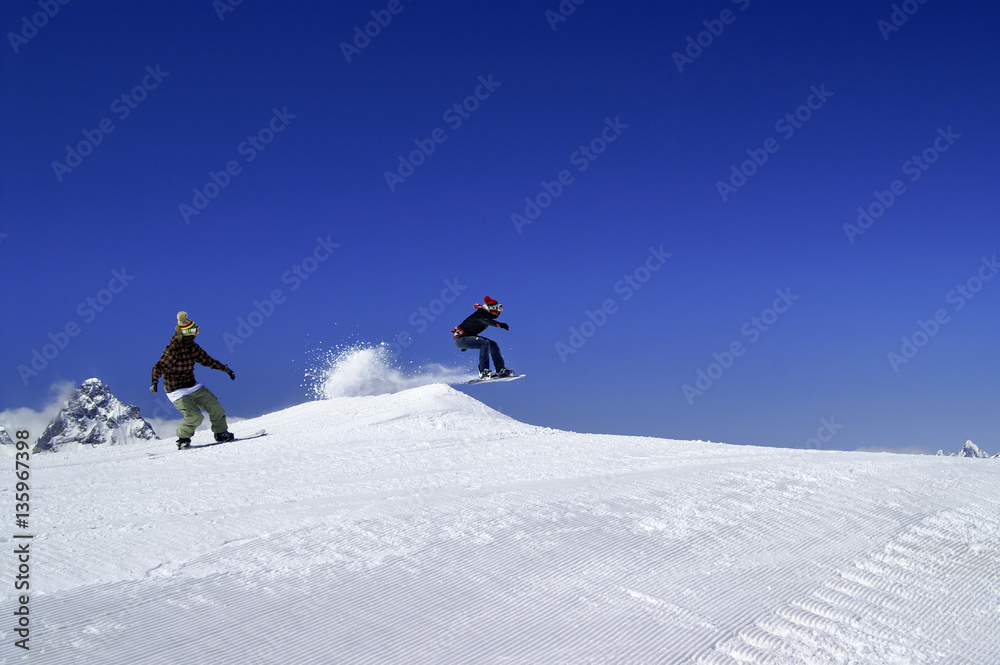 Two snowboarders jump in snow park at ski resort on sunny winter