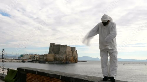 Pulcinella traditional Neapolitan mask gestures with Castel dell'Ovo in the background in the Gulf of Naples.