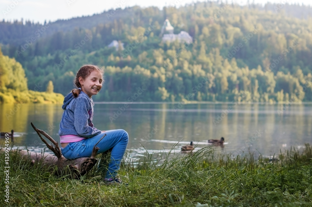 A girl child sits on the shore of a mountain lake. A girl child sits on the shore of a mountain lake.