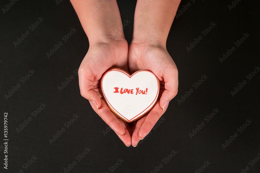 Obraz premium Beautiful gingerbread heart in the hands of the girl on a black background. Postcard for Valentine's Day, March 8, mother's Day or wedding. Free space for text