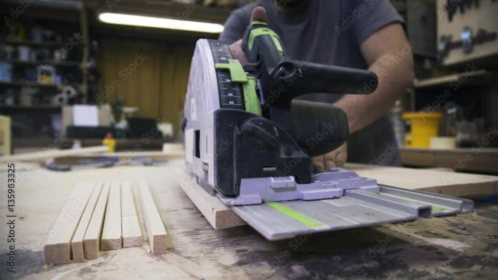 A craftsman is sawing a wooden bar using a power saw. Real time shot A craftsman is sawing a wooden bar using a power saw. Real time shot