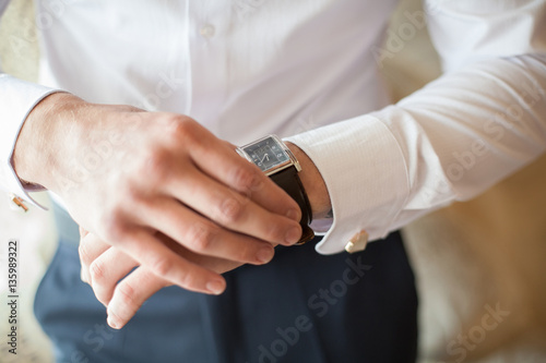 The groom in white shirt puts on a watch, close-up